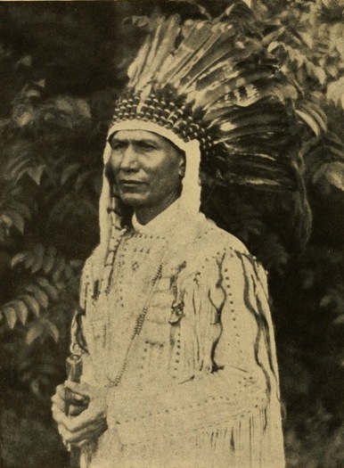 Portrait of the author, a Native American man wearing a war bonnet. The image is in black and white.