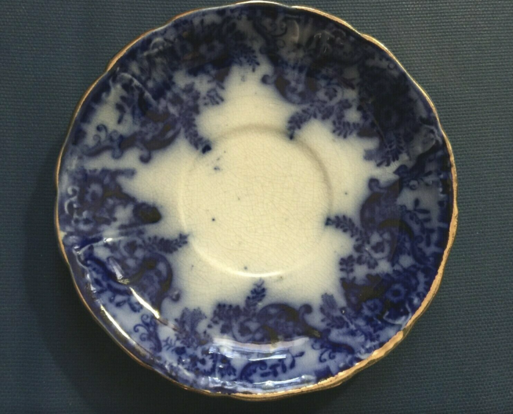 Photo of antique flow blue (blue and white, with gold edge) china saucer. Public domain.