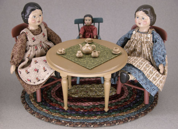 Three dolls enjoying a tea party, with oval rug and mustard colored table set  with dishes. Courtesy Gail Wilson Designs.